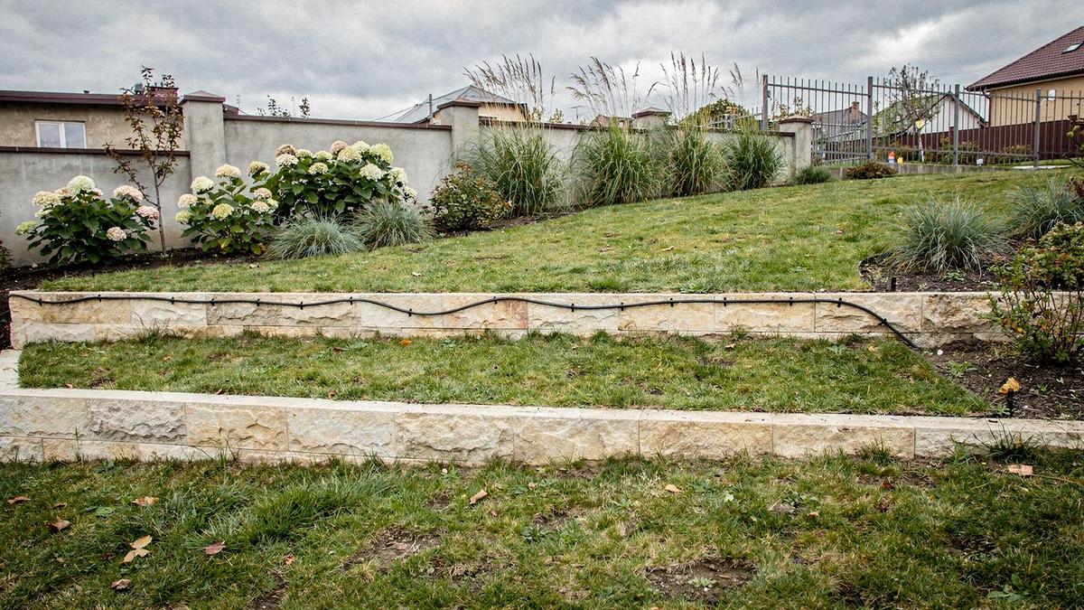 Sloped residential garden near Irpin with a graded lawn, mixed border planting and a drip irrigation line along the terrace edge